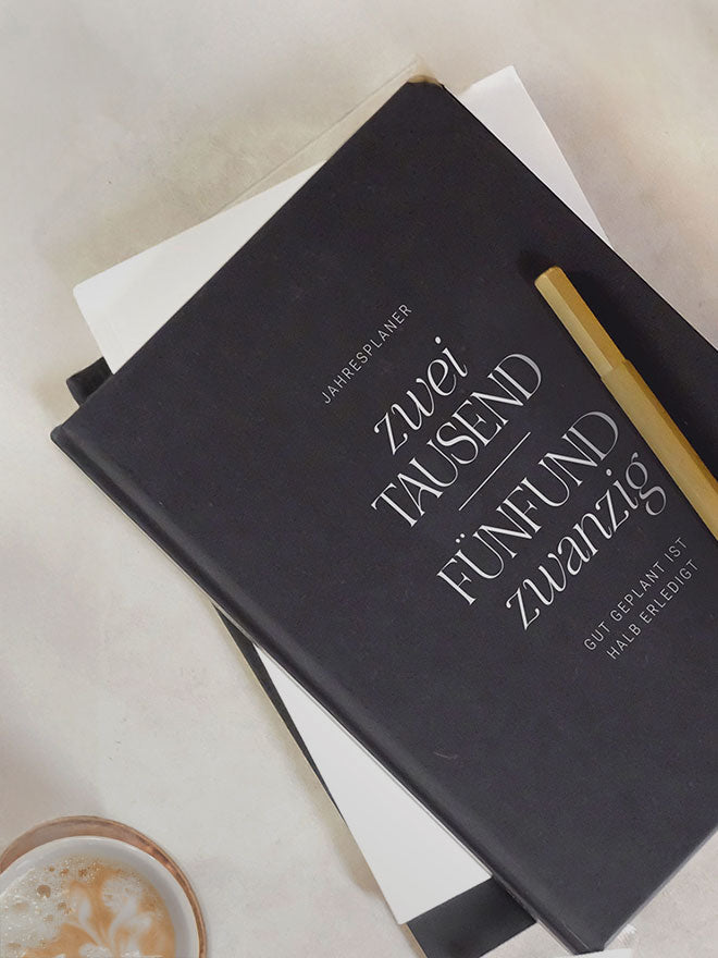 Jahresplaner Kalender von ELLY SPARKS in der black edition auf dem Tisch mit Stift und Kaffeetasse